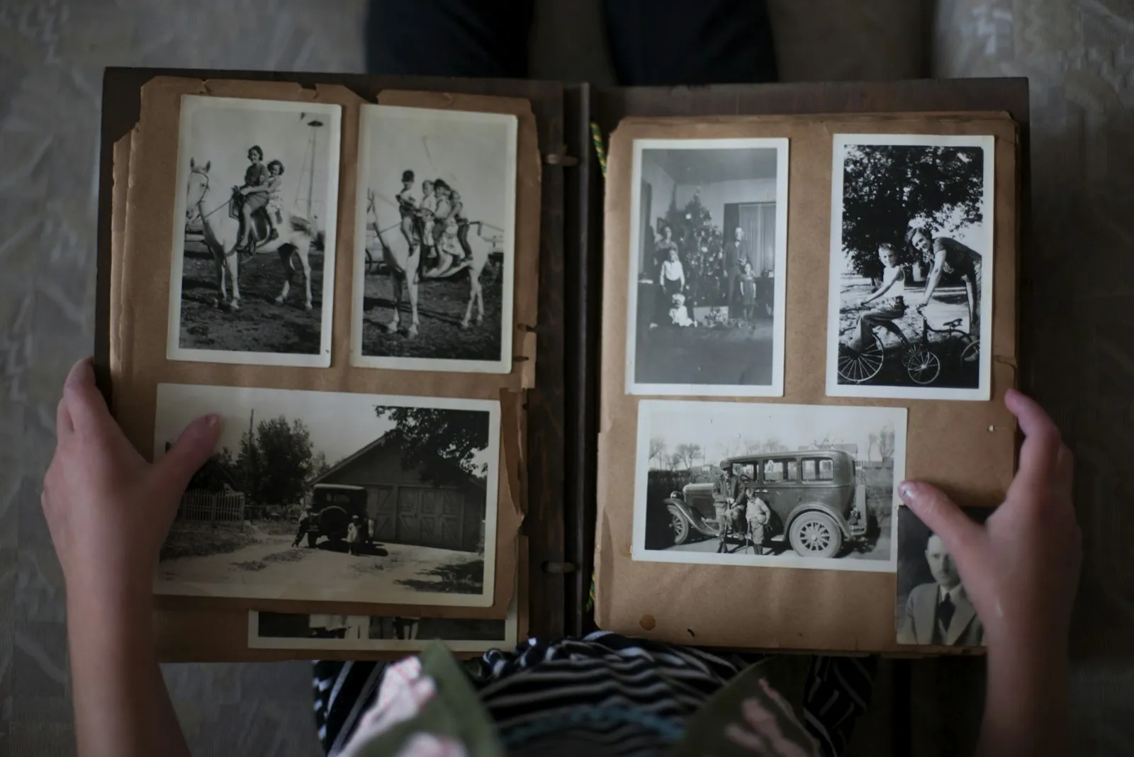 Hands holding open an old family album of black-and-white photographs